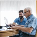 Adult grandson teaching his grandfather to use laptop